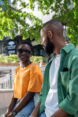 Relaxed loving african american young couple sitting near underground pass looking each other chatting enjoy sunny day in city. Interested black man talking with girlfriend rest after walking downtown