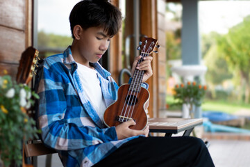 Asian preteen boy playing ukulele and acoustic guitar at home, lifestyle and hobby of children...