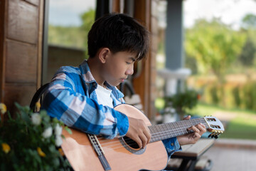 Asian preteen boy playing ukulele and acoustic guitar at home, lifestyle and hobby of children...