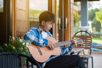 Asian preteen boy playing ukulele and acoustic guitar at home, lifestyle and hobby of children concept.