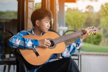 Asian preteen boy playing ukulele and acoustic guitar at home, lifestyle and hobby of children...
