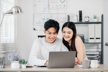 Smiling young couple working together on a laptop in a home office environment with cheerful decor.