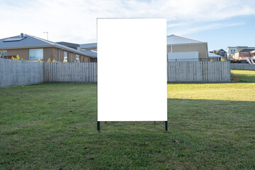 A blank white advertisement board on a vacant land in a residential suburban neighborhood. Mockup sign background texture for real estate land for sale, property investment, lot of block available.