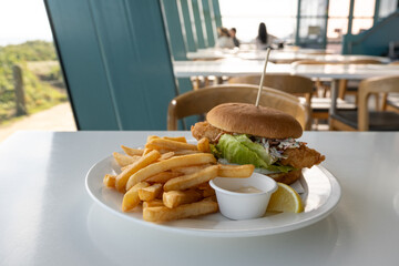 Close-up of a classic meal of a fried fish burger with some chips, a slice of lemon and dipping...