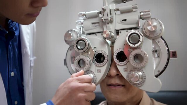 Male optician or optometrist specialist checking vision of a Senior man using examination equipment inside an optometry clinic