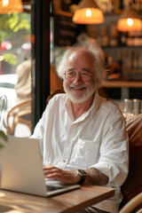 Fototapeta premium A cheerful senior man using a laptop in a cafe bathed in natural light.