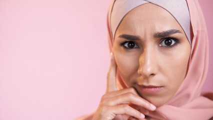 Confused face. Pensive expression. Portrait of concerned serious skeptic woman in hijab thinking isolated on pink empty space background.