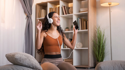 Music energy. Home joy. Sound technology. Happy amused smiling woman enjoying listening to mp3 audio in headphones using mobile phone at modern interior with copy space.