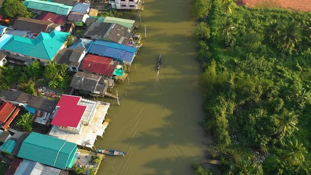 Drone tracking a traditional Kolae boat on a river in Surat Thani, sunny Thailand