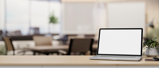A laptop computer mockup on a table with a blurred background of a contemporary meeting room.