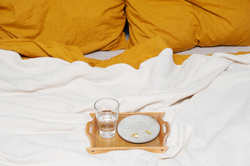 Glass of water and vitamin capsules placed on the bed.