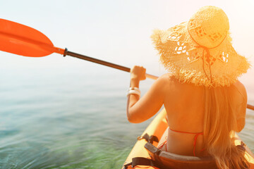 woman straw hat paddling a kayak on a lake. The sun is shining brightly, creating a warm and...