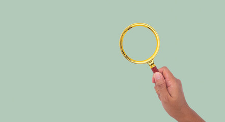 Close-up of a woman's hand holding a magnifying glass against a green background.