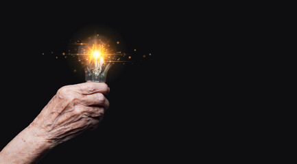 Close-up of a senior woman's hand holding a light bulb with illuminating ideas on a black...