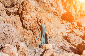 Woman green dress sea. Woman in a long mint dress posing on a beach with rocks on sunny day. Girl on the nature on blue sky background.