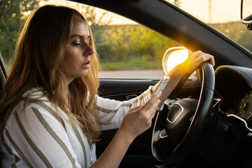 Naklejka premium Womandriver using mobile phone paying for parking and navigating in the city while stopped on the side of the road. Self road trip, technology, travel and people concept