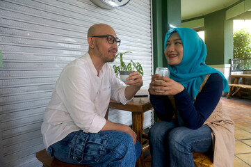 Asian couple sitting in a cafe looking at each other, enjoying coffee and conversation. Love and...