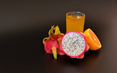 A glass of a mixture of fruit juices on a black background, next to a half of a ripe orange and a pitaya.