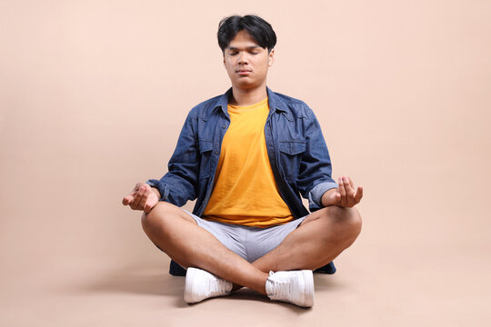 Full Length Of Young Asian Man Sitting For Meditation Isolated On Beige Background