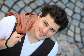 portrait of a handsome confident young man with brown leather jacket on a street