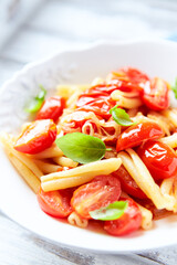 Casarecce pasta withe cherry tomatoes and fresh basil. Bright wooden background. Close up.	