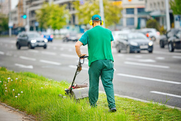 Man cutting grass with lawnmower, trimming grass and mowing along the road. Utility worker trim...