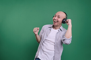 Asian bald man listening music with headphones and clenching fist dancing to the rhythm