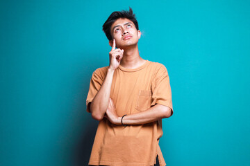 Young Asian guy put hand on head and looking up thinking of something isolated on teal background