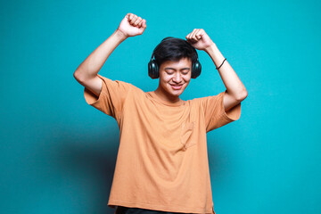 Asian man listening music with headphones and clenching fist dancing to the rhythm