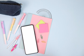 Smartphone with blank screen with school stationery on pastel background. Back to school concept. 