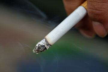 A man's hand holds a burning cigarette. He smokes.