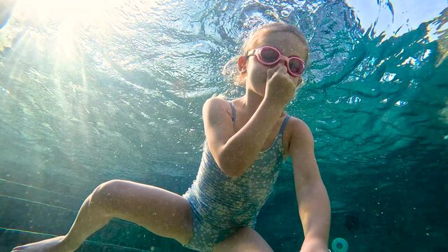 Child girl in a swimming pool learns to dive and swim. Kid diving underwater swimming pool summer. 