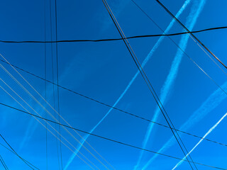 Pattern of airplane contrails and electrical wires over blue sky in spring