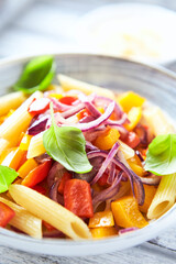 Penne pasta with yellow and red pepper, hard cheese and fresh basil. Bright background. Close up.