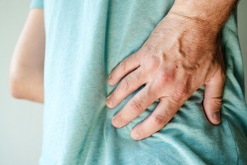 Back pain symptoms, close up of male hand holding the painful sport on lower back loin