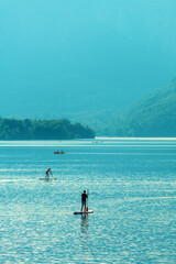 Water sport activities on lake Bohinj in summer, people rowing boats and paddling on standup boards