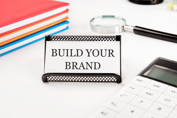 Branding rebranding marketing business concept. BUILD YOUR BRAND words on a business card in a composition with a calculator, notebooks and a magnifying glass