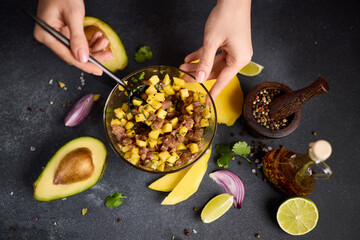 Woman mixing chopped tuna, mango, cilantro and onion in a glass bowl cooking traditional tuna and mango tartare