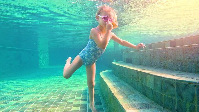 Child girl in a swimming pool learns to dive and swim. Kid diving underwater swimming pool summer. 