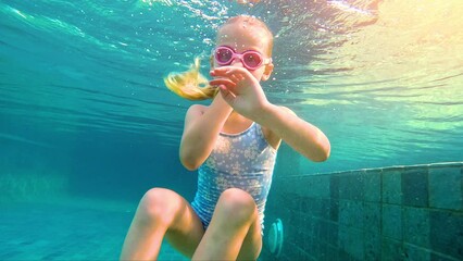 Girl swimming underwater in the pool. Cute little girl with goggles diving and swimming underwater in a pool. 