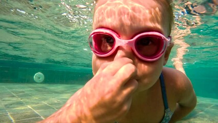 Girl swimming underwater in the pool. Cute little girl with goggles diving and swimming underwater in a pool. 