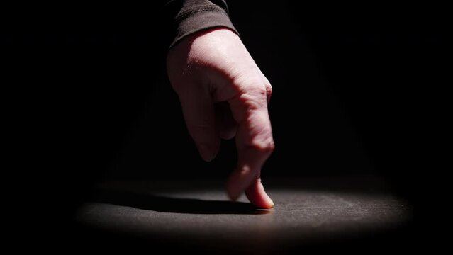 Dancing fingers of man's hand moonwalking with stage lighting on black background close-up.