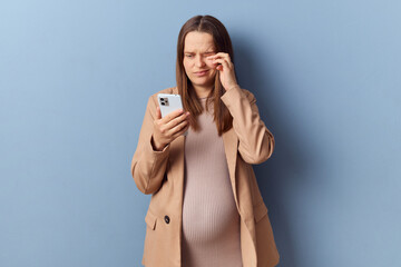 Sad tired young adult pregnant woman wearing dress and jacket posing isolated over blue background...