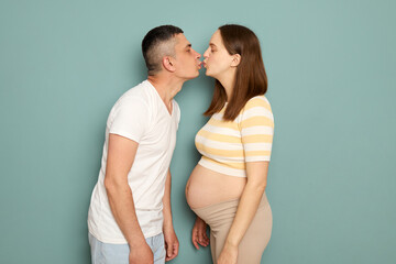 Loving Caucasian young married pregnant family standing isolated over light green background...