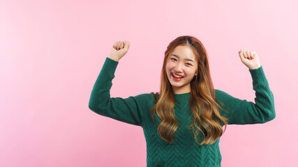 Young women raising arms with winner gesture and smiling with happiness isolated on pink background