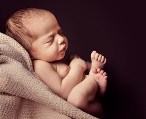 Newborn sleeping on Blanket over black background. Baby sleep in Fetal position Side view. Infant...