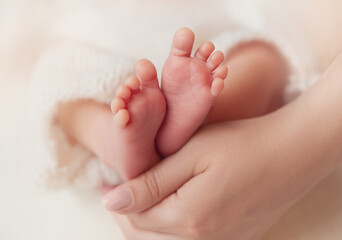 Baby Feet in Mother Hands. Newborn Toes Close up over White Soft background. Mum holding Tiny Feet with Love. Maternity and Childcare Concept