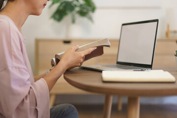 Female entrepreneur reading a book and working to searching business data on laptop at home