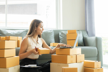 Small business startup, SME owner, female entrepreneur working on receipt boxes and checking online orders, laptop to prepare to pack boxes to sell to customers. Close-up photo