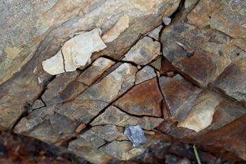 Photo of stone texture. Macro. Various shades of brown, orange, red, gray and white. Stones of different sizes. They have black cracks and crevices. Chaotic placement.